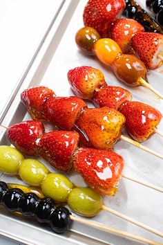 fruit skewers are lined up on a tray with olives and strawberries