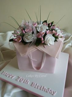 a pink gift bag with white and pink flowers on it is sitting next to a card that says happy 70th birthday