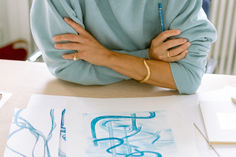 a woman sitting at a table with her arms folded over her chest and drawing on paper