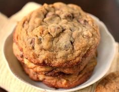 three chocolate chip cookies stacked on top of each other in a white bowl next to a brown napkin