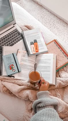 a person is sitting on a bed with books, notebooks and a cup of coffee