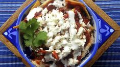 a blue bowl filled with mexican food on top of a tablecloth covered table next to utensils