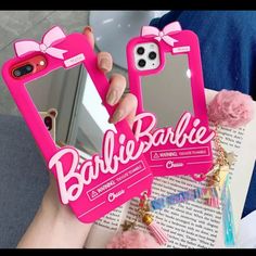 someone holding up two cell phones with pink cases and bows on the front, while another holds