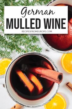 two mugs filled with mulled wine next to orange slices and cinnamonsticks