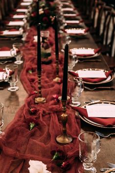 a long table is set with place settings and red linens for the runneres