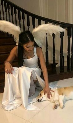 a woman kneeling down next to a dog with angel wings on it's head