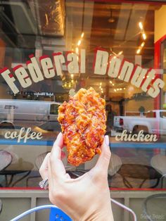 a hand holding up a piece of pizza in front of a restaurant window with the words federal donuts on it