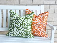 two orange and green pillows sitting on top of a white bench next to a brick wall