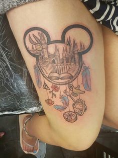 a woman's thigh with a mickey mouse tattoo on her leg and an image of a castle in the background