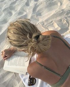 a woman sitting in the sand reading a book