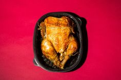 a whole chicken in a roasting pan on a pink background