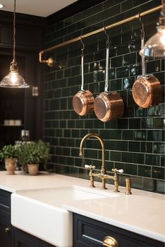 copper pots and pans hang on the wall above a kitchen sink with black cabinets