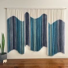 two blue and white curtains hanging on a wall next to a plant in a pot