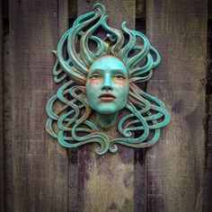 a green mask is mounted on a wooden wall with an intricate pattern around it's face