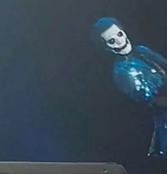 a man with blue hair and a skeleton face on his head is standing in front of a laptop