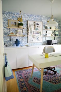 a room with blue and white wallpaper has a desk in the corner, shelves on either side