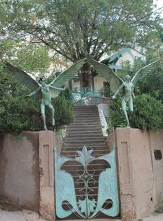 an iron gate with two winged statues on it and steps leading up to the entrance