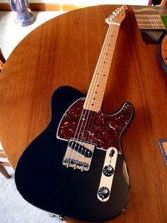 a black guitar sitting on top of a wooden table