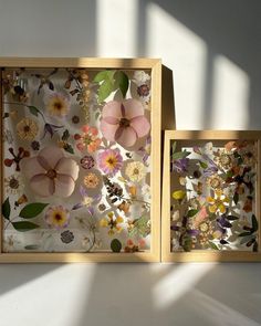 two wooden frames with flowers on them in front of a white wall and shadows from the window