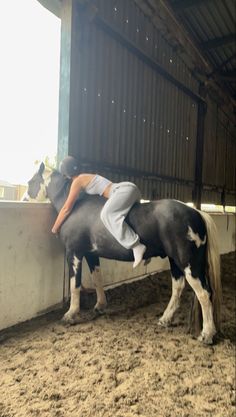 a woman is sitting on top of a black and white horse in an enclosed area