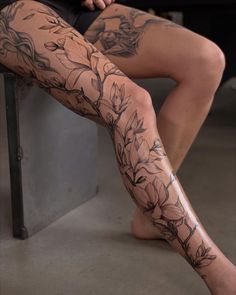 a woman's legs with tattoos and flowers on them sitting next to a wall