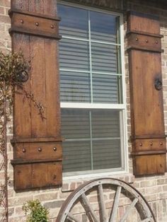 an old wagon wheel sits in front of a brick building with shutters and windows