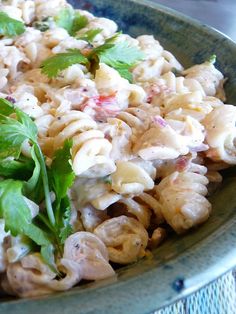 a green bowl filled with pasta salad and garnished with cilantro leaves