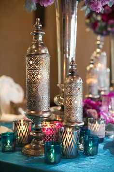 a table topped with vases filled with purple flowers and lit candle holders next to each other