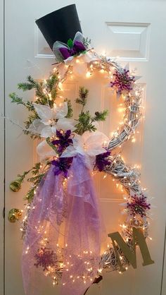 a wreath with purple and white flowers is hanging on the front door, decorated with lights