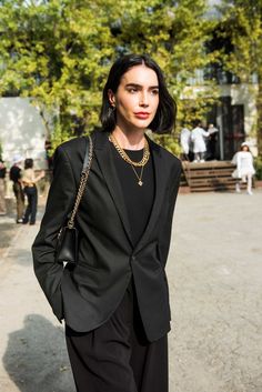 a woman with black hair wearing a black suit and holding a handbag in front of her