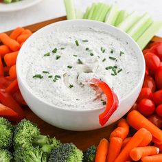 a bowl of dip surrounded by carrots, broccoli and celery