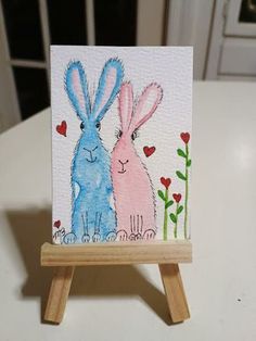 a card with two blue and pink rabbits sitting on top of a wooden easel