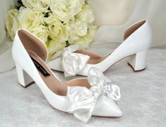 a pair of white high heels with a bouquet of flowers in the background