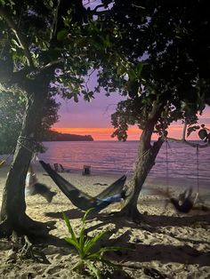 a hammock hanging between two trees on the beach at sunset with people in the background