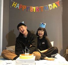 two people sitting on a bed with a birthday cake