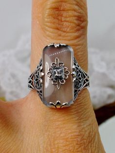 Frosted Camphor Glass Solid Sterling Silver Ring Grace Design#D233 This is a lovely antique Edwardian era inspired filigree ring. This gorgeous ring is created in stunning frosted camphor glass. The glass is embellished with a delicate floral filigree. The top of the ring holds a center set 1mm round cut gemstone (Choose from white Cubic Zirconia, lab created Moissanite, or Natural/Genuine White Diamond). The frosted glass is 18mm x 19mm. The ring sits 18mm north-south and 10mm east-west on the Vintage Silver Ring With Intaglio, Vintage Silver Intaglio Rings, Vintage Carved Filigree Ring Gift, Carved Vintage Filigree Ring Gift, Art Deco Silver Ring With Intaglio, Vintage White Filigree Ring With Intricate Design, Elegant Carved Filigree Ring For Anniversary, Antique Carved Filigree Ring For Wedding, Vintage Oval Carved Filigree Ring