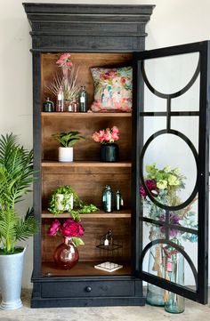 an old china cabinet is decorated with flowers and plants in vases on the shelves