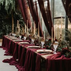 a long table is set with place settings and red cloth draped over it, along with candles