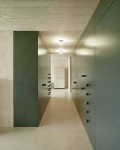 a long hallway with green cabinets and white walls is lit by recessed lights on either side