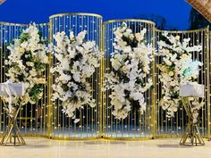 three tall white flowers are on display in front of a gold fence with lights behind them