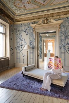 a person sitting on a bed in a room with blue and white wallpapers