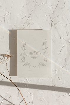 a wedding card laying on top of a piece of paper next to some dried flowers