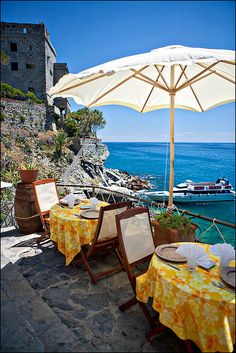 an outdoor dining area with yellow table cloths and white umbrella over the tables overlooking the ocean