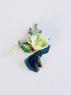 a boutonniere with white flowers and green leaves on a blue ribbon tied around it