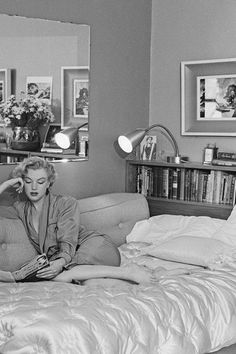 a black and white photo of a woman sitting on a bed in a bedroom with bookshelves