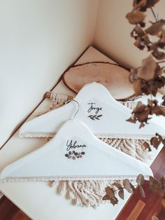 two white hangers with embroidered names on them sitting next to some dried leaves and branches