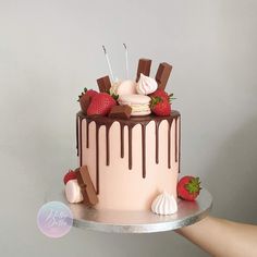 a hand holding a cake with chocolate and strawberries on the top that is covered in icing