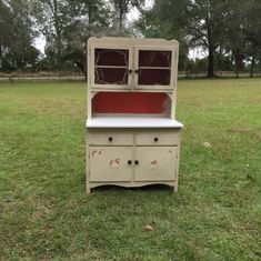 an old china cabinet sitting in the middle of a field with grass and trees behind it