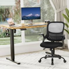 a desk with a computer on it in front of a window and a potted plant