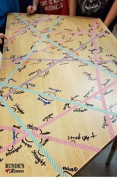 a wooden table covered in writing on top of a white board with people standing around it